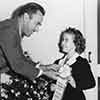 Shirley Temple receiving her Rose Parade Grand Marshal ribbon from Tournament Chairman Lathrop K. Leishman at her Fox Bungalow, November 21, 1938